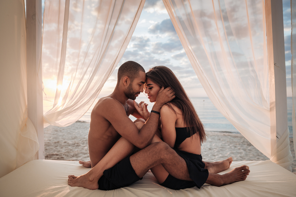 Passionate,Young,Couple,Sitting,In,Bed,On,The,Beach